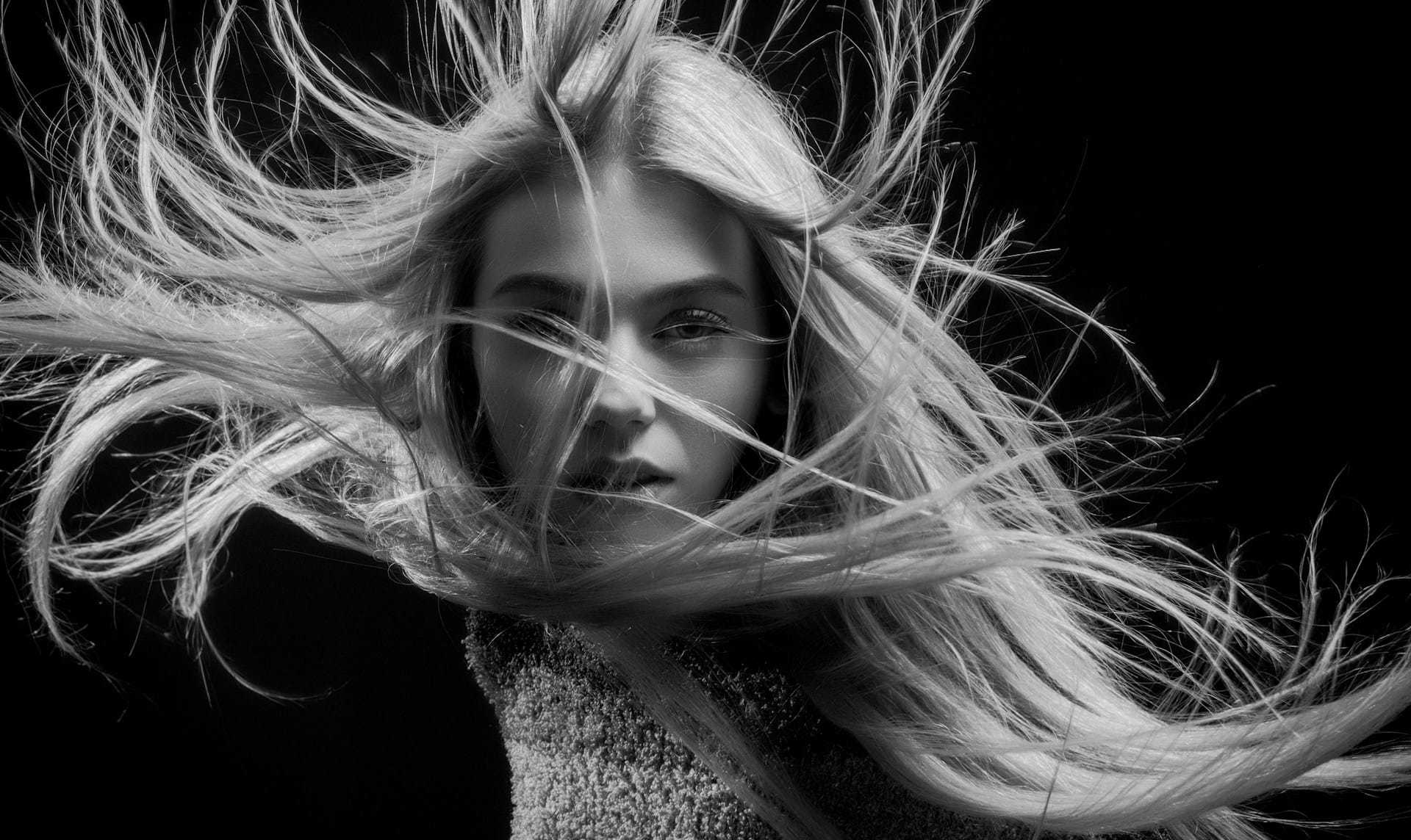 Wind-swept blonde woman in dramatic black-and-white portrait.