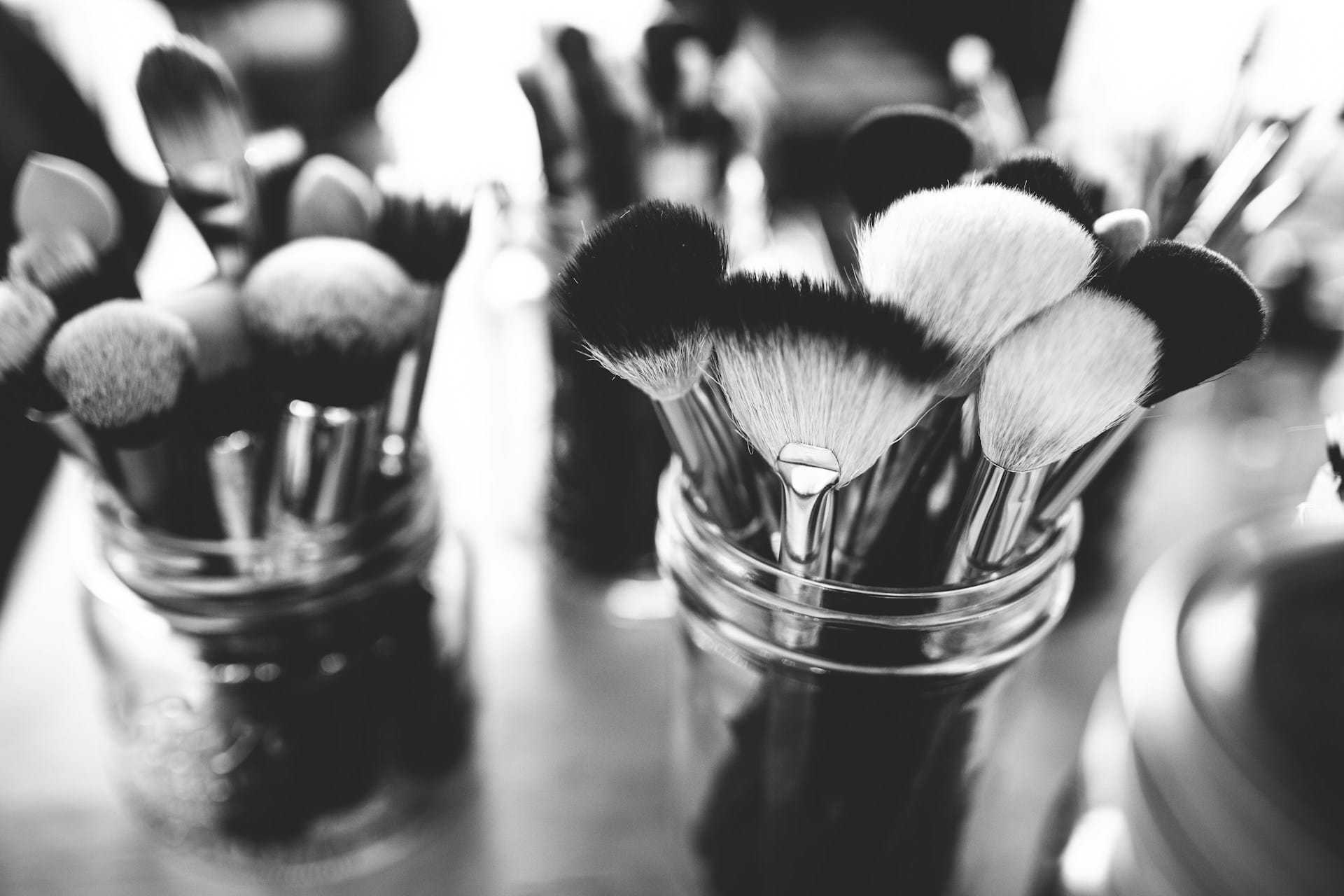 Makeup brushes in glass jars on a table, black and white photo.
